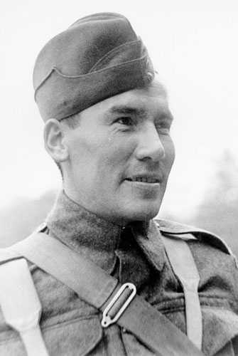 Photographie en noir et blanc – Harvey Dreaver regardant au loin, photographié à partir de la poitrine. Il porte l’uniforme complet, y compris la casquette. Une sangle traverse sa poitrine.